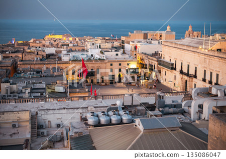 A stunning aerial view of Valletta's rooftops, showcasing the city's historic architecture, domes, and limestone buildings under the Mediterranean sky. A stunning aerial view of Valletta's rooftops, showcasing the city's historic architecture, domes, and limestone buildings under the Mediterranean sky. 135086047