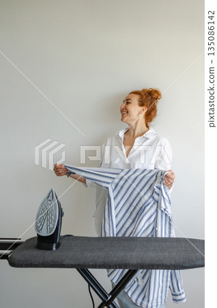 Young woman using ironing board to press clothes neatly at home. Young woman using ironing board to press clothes neatly at home. 135086142