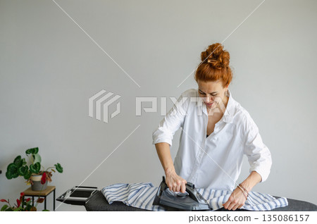 Young woman using ironing board to press clothes neatly at home. Young woman using ironing board to press clothes neatly at home. 135086157