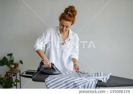 Young woman using ironing board to press clothes neatly at home. 135086159