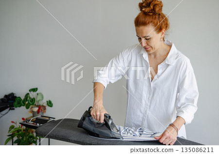 Young woman using ironing board to press clothes neatly at home. Young woman using ironing board to press clothes neatly at home. 135086211