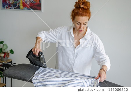 Young woman using ironing board to press clothes neatly at home. Young woman using ironing board to press clothes neatly at home. 135086220