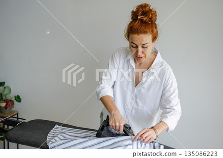 Young woman using ironing board to press clothes neatly at home. 135086223