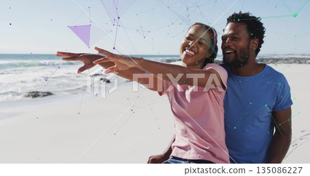 Couple sitting on sandy beach extending arms forward, with pink and light blue t-shirts and jeans Couple sitting on sandy beach extending arms forward, with pink and light blue t-shirts and jeans 135086227