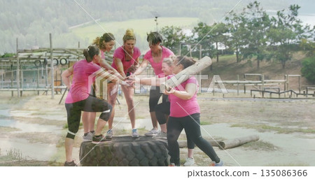 Group of women in pink sportswear gathering at obstacle course, with tractor tire and wooden log 135086366