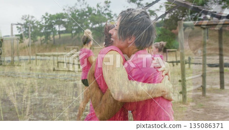 Hugging teammates wearing pink athletic tops on obstacle field, with wooden posts and metal frames 135086371