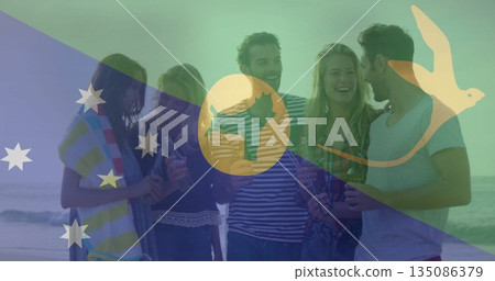 Friends in swimwear holding beer bottles on sandy beach, with towel and Australian flag graphic 135086379
