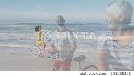Three-generation family cycling and standing on beach, smiling with pink cruiser and black bicycles Three-generation family cycling and standing on beach, smiling with pink cruiser and black bicycles 135086396