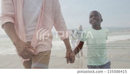 Walking father wearing light pink shirt with son in pale-green shirt holding hands on shoreline Walking father wearing light pink shirt with son in pale-green shirt holding hands on shoreline 135086415