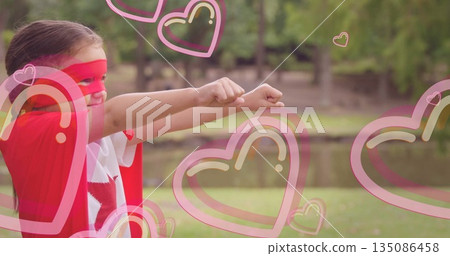 Pretending child wearing cape and mask flying in park by pond, with heart overlays, copy space Pretending child wearing cape and mask flying in park by pond, with heart overlays, copy space 135086458