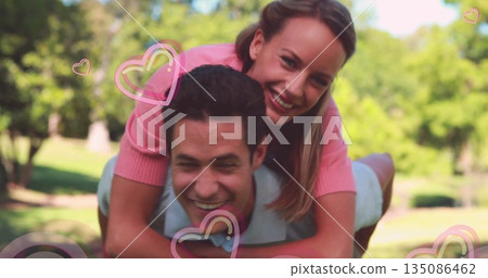 Carrying couple wearing grey polo and pink top posing in sunlit park, with pink heart graphics Carrying couple wearing grey polo and pink top posing in sunlit park, with pink heart graphics 135086462
