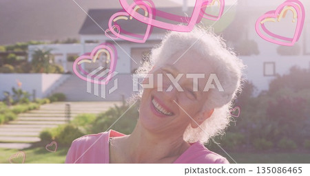 Smiling senior woman wearing pink top standing on concrete steps of white house, with heart icons Smiling senior woman wearing pink top standing on concrete steps of white house, with heart icons 135086465