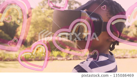Boy exploring virtual world wearing headset in sunlit garden, with pink heart overlays, copy space Boy exploring virtual world wearing headset in sunlit garden, with pink heart overlays, copy space 135086469