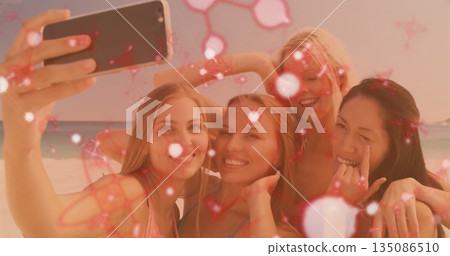 Smiling group of women in colorful bikinis holding smartphone for beach selfie with sparkle overlay Smiling group of women in colorful bikinis holding smartphone for beach selfie with sparkle overlay 135086510