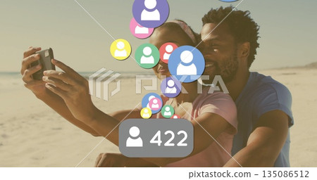Taking selfie Black couple hugging at beach edge, with smartphone, floating avatars and 422 badge 135086512