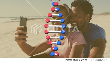 Taking selfie couple embracing on sandy beach by ocean, with smartphone and DNA helix 135086513