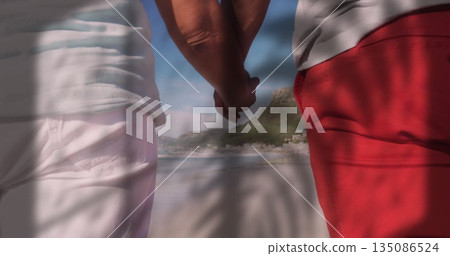 Holding hands couple standing at sandy beach shoreline, with palm frond patterns 135086524