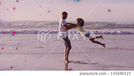 Spinning striped T shirt father lifting daughter into twirl at beach shoreline, with ocean waves Spinning striped T shirt father lifting daughter into twirl at beach shoreline, with ocean waves 135086525