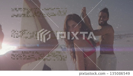 Smiling trio of friends wearing swimwear standing at water's edge with three surfboards 135086549