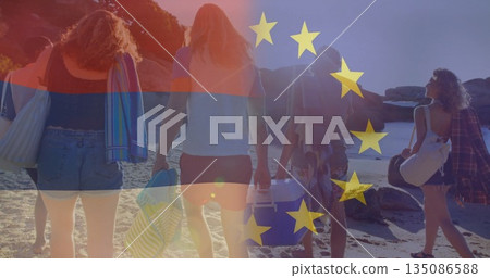 Walking five friends along sandy beach carrying cooler, striped towels, canvas totes and blanket 135086588