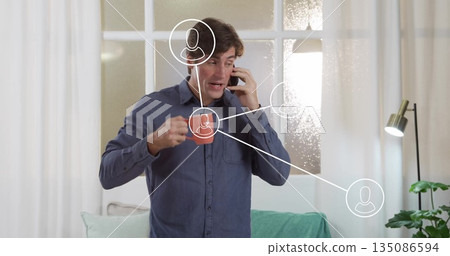 Talking on smartphone, man gesturing in living room with frosted window, digital connection icons 135086594