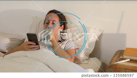Lying mid adult female checking smartphone in duvet in bedroom, with envelope icon and thermometer Lying mid adult female checking smartphone in duvet in bedroom, with envelope icon and thermometer 135086597