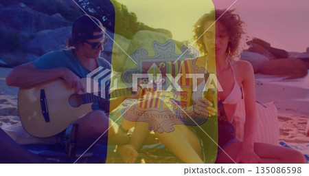 Strumming acoustic guitar and ukulele, friends in swimwear sharing bottled drink on beach blanket 135086598