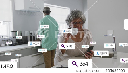 Senior woman checking smartphone notifications and holding mug at kitchen island, digital overlays Senior woman checking smartphone notifications and holding mug at kitchen island, digital overlays 135086603