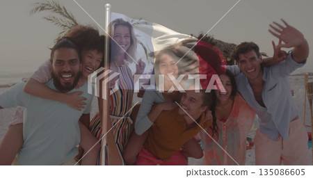 Posing group of friends giving piggyback rides on sandy shore, with flagpole and tiki torches 135086605