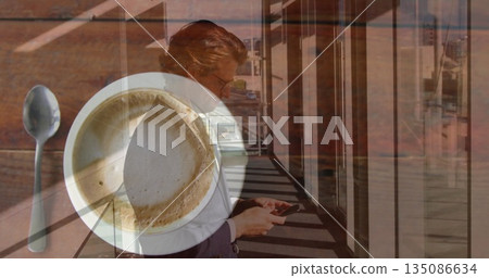 Business executive in blazer checking messages on smartphone in corridor, with coffee cup and spoon Business executive in blazer checking messages on smartphone in corridor, with coffee cup and spoon 135086634