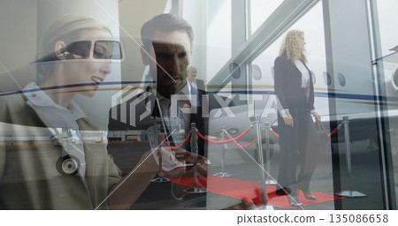 Scanning boarding pass on smartphone, executive standing by private jet with red carpet stanchions 135086658
