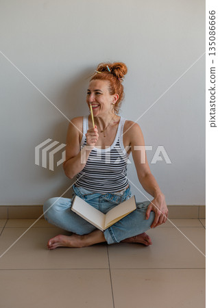 Portrait of a thoughtful girl holding a pen and notebook, looking aside, searching for inspiration. 135086666