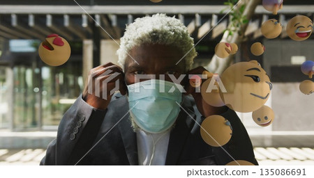 Businessman adjusting mask wearing suit and earphones in transit station, with floating emoji icons Businessman adjusting mask wearing suit and earphones in transit station, with floating emoji icons 135086691