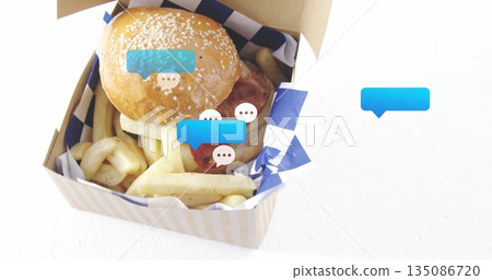 Displaying takeout box holding burger and fries on kitchen countertop with chat bubbles, copy space 135086720