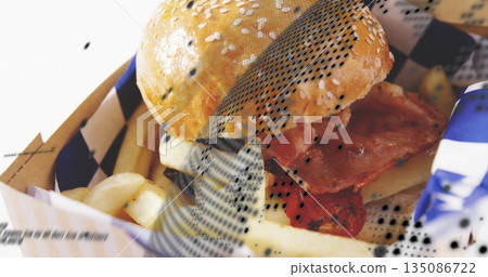 Presenting sesame-seed bacon cheeseburger in cardboard tray, with golden fries and checkered liner 135086722