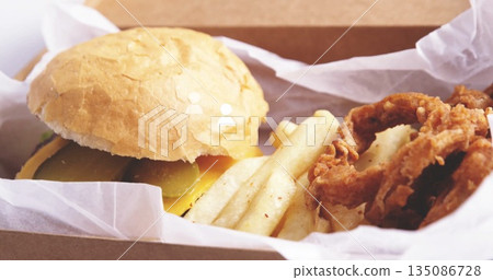 Takeout meal resting in box on table, with cheeseburger, pickles, fries, onion rings, copy space Takeout meal resting in box on table, with cheeseburger, pickles, fries, onion rings, copy space 135086728