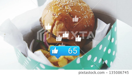 Sesame-seed burger nestling in teal-polka-dot box on table, with fries, floating likes counting 65 Sesame-seed burger nestling in teal-polka-dot box on table, with fries, floating likes counting 65 135086745
