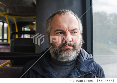 Portrait of an elderly European man sitting inside a tram, calmly waiting for his stop. Casual everyday scene, thoughtful expression, public transport interior, urban atmosphere, soft daylight through Portrait of an elderly European man sitting inside a tram, calmly waiting for his stop. Casual everyday scene, thoughtful expression, public transport interior, urban atmosphere, soft daylight through 135086771
