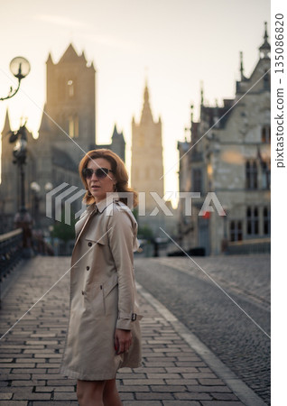 Elegant, well-groomed woman with fashionable style strolling around the city in a beige coat and sunglasses. Looking confident and sophisticated. Elegant, well-groomed woman with fashionable style strolling around the city in a beige coat and sunglasses. Looking confident and sophisticated. 135086820