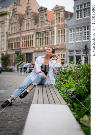 Elegant, well-groomed woman with fashionable style strolling around the city in a white shirt and jeans and sunglasses. Looking confident and sophisticated. 135086906