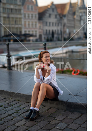 Elegant, well-groomed woman with fashionable style strolling around the city in a white shirt, little black dress and sunglasses. Looking confident and sophisticated. 135086914