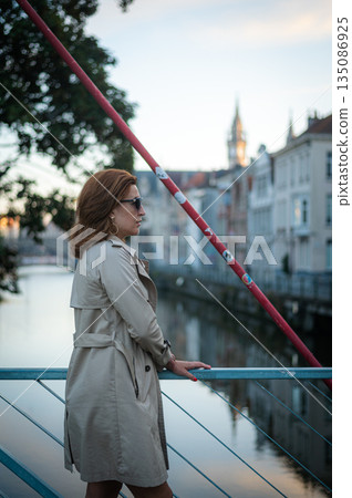 Elegant, well-groomed woman with fashionable style strolling around the city in a beige coat and sunglasses. Looking confident and sophisticated. Elegant, well-groomed woman with fashionable style strolling around the city in a beige coat and sunglasses. Looking confident and sophisticated. 135086925