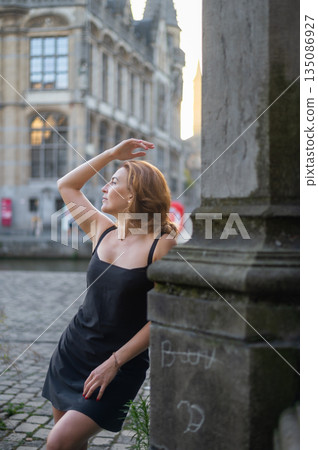 Elegant, well-groomed woman with fashionable style strolling around the city at early morning in a little black dress and sunglasses. Looking confident and sophisticated. Elegant, well-groomed woman with fashionable style strolling around the city at early morning in a little black dress and sunglasses. Looking confident and sophisticated. 135086927