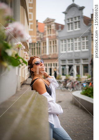 Elegant, well-groomed woman with fashionable style strolling around the city in a white shirt and jeans and sunglasses. Looking confident and sophisticated. 135086928