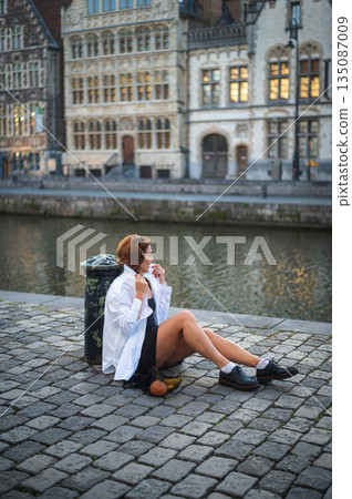Elegant, well-groomed woman with fashionable style strolling around the city in a white shirt, little black dress and sunglasses. Looking confident and sophisticated. Elegant, well-groomed woman with fashionable style strolling around the city in a white shirt, little black dress and sunglasses. Looking confident and sophisticated. 135087009