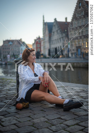Elegant, well-groomed woman with fashionable style strolling around the city in a white shirt, little black dress and sunglasses. Looking confident and sophisticated. Elegant, well-groomed woman with fashionable style strolling around the city in a white shirt, little black dress and sunglasses. Looking confident and sophisticated. 135087062