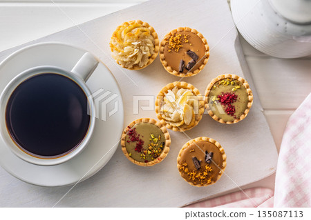 Sweet mini tartlets and coffee cup on white table. Top view. 135087113