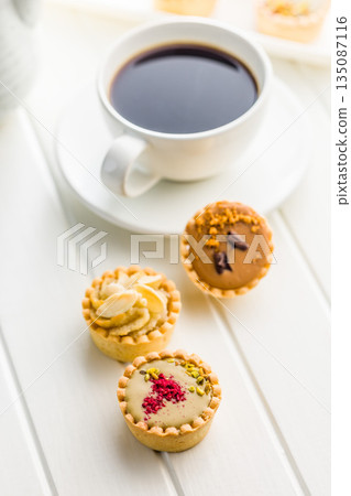 Sweet mini tartlets and coffee cup on white table. Sweet mini tartlets and coffee cup on white table. 135087116