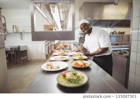 African American male chef arranging dishes under heating lamp on steel kitchen counter, copy space African American male chef arranging dishes under heating lamp on steel kitchen counter, copy space 135087301