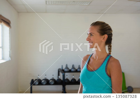 Adult woman smiling near kettlebells and green exercise mat by window at fitness studio, copy space Adult woman smiling near kettlebells and green exercise mat by window at fitness studio, copy space 135087328